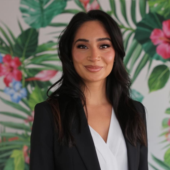 Jas, content creator for Destinations by Easy Weddings, in a tailored black blazer against a tropical floral backdrop
